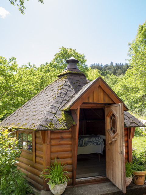 Kleine Holzhütte mit Moosdach, offene Tür und Zimmerpflanzen am Eingang, Campsite Des Randonneurs, Occitanie.