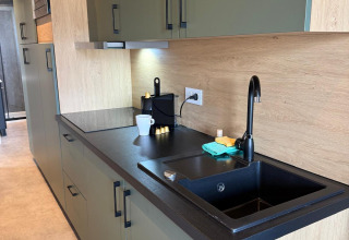 Cucina moderna con mobili verdi, lavello nero e macchina da caffè presso Mobi Lodge, Arden Parks Tulderheyde, Belgio.