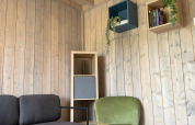 Moderne lounge på Mobi Lodge i Arden Parks Tulderheyde, Belgien med sofa, stol og træinteriør.