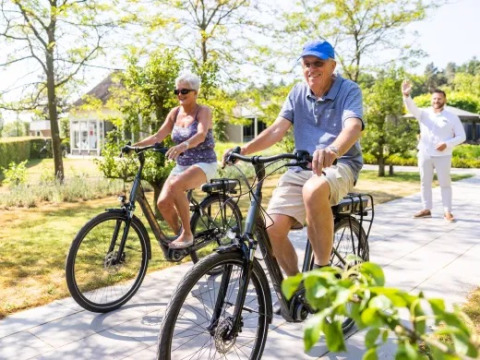 Ældre par cykler på feriepark Molenvelden i North-Brabant, Nederlandene, på en solrig dag.
