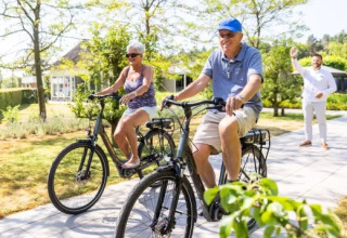 Coppia anziana in bicicletta al parco vacanze Molenvelden nel North-Brabant, Paesi Bassi, in una giornata di sole.