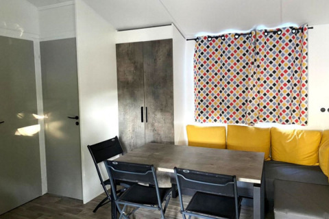 Eethoek met grijze tafel, zwarte stoelen, gele kussens en bont gordijn in Comfort Mobile home Frankrijk.
