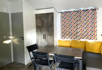 Eethoek met grijze tafel, zwarte stoelen, gele kussens en bont gordijn in Comfort Mobile home Frankrijk.