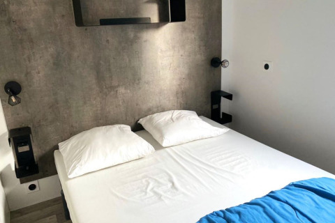 Moderne glampingkamer met een betonnen muur, dubbel bed met witte kussens en een blauwe deken.