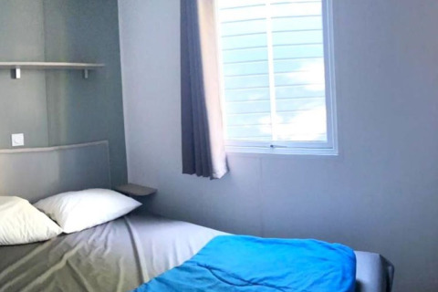 Kleine slaapkamer met bed, witte kussens en raam in Comfort Mobile Home bij Camping Paradis Family des Issoux, Frankrijk.