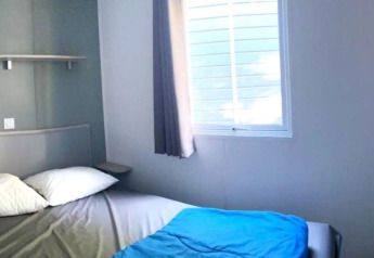 Pequeño dormitorio con cama, almohadas blancas y ventana en Comfort Mobile Home en Camping Paradis Family des Issoux, Francia.