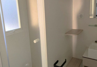 Kleine badkamer met witte deur, lavabo, spiegel en zwarte wc-rolhouder in een Franse mobielhome.