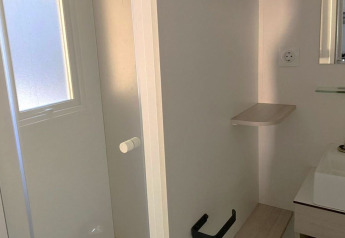 Kleines Badezimmer mit weißer Tür, Waschbecken, Spiegel und schwarzem Toilettenpapierhalter in Frankreich.