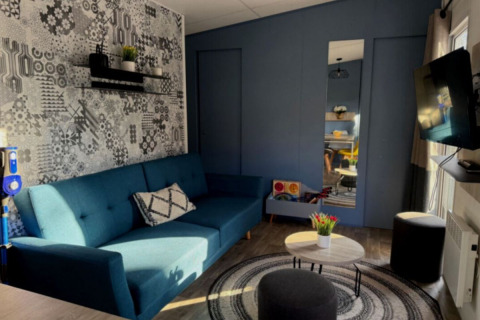 Gezellige woonkamer met blauwe zitbank en TV in Paradijs Luxe Stacaravan op Camping Paradis des Issoux.