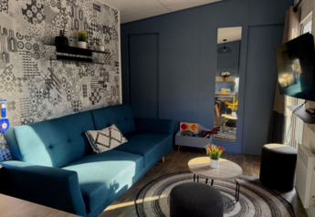 Gezellige woonkamer met blauwe zitbank en TV in Paradijs Luxe Stacaravan op Camping Paradis des Issoux.