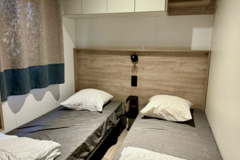 Tweepersoonskamer met grijze lakens en houten details in Paradijs Luxe Stacaravan, Camping Paradis Family des Issoux.