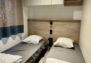 Tweepersoonskamer met grijze lakens en houten details in Paradijs Luxe Stacaravan, Camping Paradis Family des Issoux.