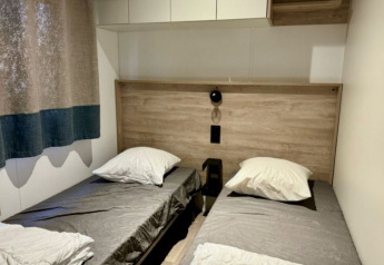 Værelse med to enkeltsenge, træpaneler, gråt sengetøj og moderne indretning på Paradijs Luxe Stacaravan.