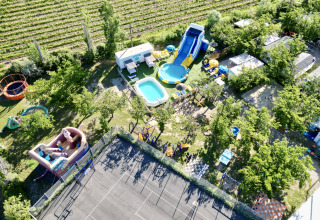 Aerial view of Camping Paradis Les Rives de l'Hérault, showing pools, slides, and a play area among trees.