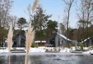 Winter scene at Holiday park Latour in North Brabant, Netherlands, with snowy lodges and a pond fountain.