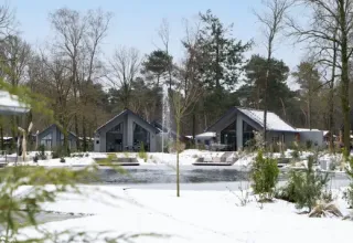 Ferienpark Latour in Nordbrabant, Niederlande, im Winter mit Schnee, Teich und modernen Hütten.
