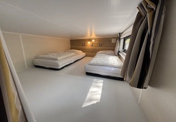 Coin nuit en mezzanine avec deux lits bas, fenêtre et rideaux dans le Tiny House au Parc de Paalberg, Pays-Bas.