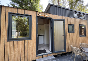 Vue extérieure d'une tiny house au Recreation Park de Paalberg aux Pays-Bas avec terrasse et chaises.