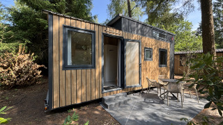 Tiny wooden house with patio and outdoor chairs in the forest, Tiny House at Recreation Park de Paalberg, Netherlands.