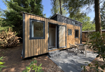 Petite maison en bois avec terrasse et chaises extérieures dans la forêt, Tiny House au Parc de Loisirs de Paalberg, Pays-Bas.