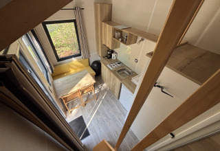 Udsigt ovenfra af et kompakt tiny house med køkken, spisebord og store vinduer i Recreation Park de Paalberg.