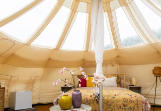 Interieur van een Lotus Belle tent bij De Achterste Hoef met gezellig bed, vazen en nachtkastje.
