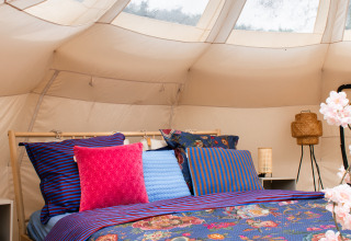 Kleurrijk bed met bloemenbeddengoed in een Lotus Belle safaritent bij De Achterste Hoef, Nederland.