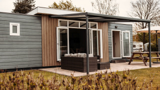 Exterior view of a luxury chalet with covered terrace, outdoor seating area, and a large picnic table.