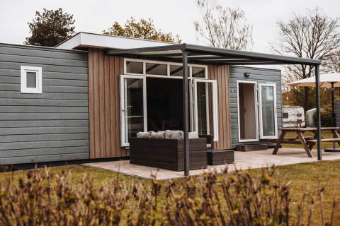 Außenansicht eines luxuriösen Chalets mit überdachter Terrasse, Gartensofa und Picknicktisch.