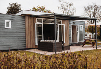 Exterior view of a luxury chalet with covered terrace, outdoor seating area, and a large picnic table.