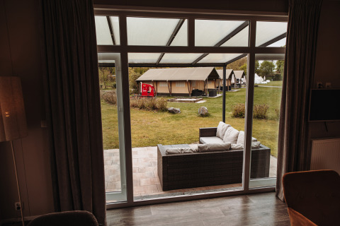 Vue depuis un chalet de luxe au parc De Achterste Hoef, Pays-Bas, terrasse aménagée et tentes à l’extérieur.