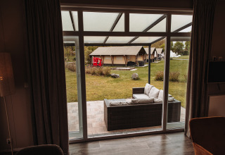 Vue depuis un chalet de luxe au parc De Achterste Hoef, Pays-Bas, terrasse aménagée et tentes à l’extérieur.