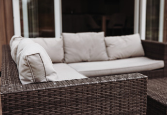 Wicker patio sofa with light cushions on the terrace at a luxury chalet in De Achterste Hoef, Netherlands.