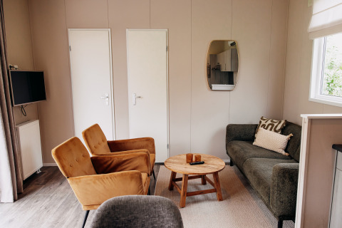 Salon moderne de chalet avec fauteuils moutarde, canapé gris, table en bois et TV à De Achterste Hoef.