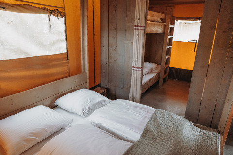 Interior of a safari tent featuring a double bed and bunk beds at Recreation park De Achterste Hoef, Netherlands.