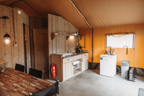 Intérieur d'une tente safari avec cuisine, réfrigérateur et table à Recreation park De Achterste Hoef, Pays-Bas.