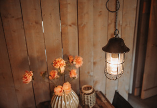 Hængende lampe og vase med blomster på træbord i safaritelten på De Achterste Hoef i Holland.