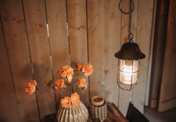 Hængende lampe og vase med blomster på træbord i safaritelten på De Achterste Hoef i Holland.