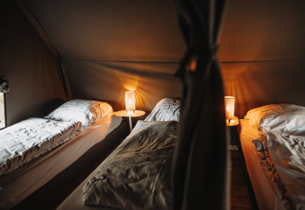 Trois lits simples avec draps blancs et lampes chaleureuses dans une lodge à De Achterste Hoef, Pays-Bas.