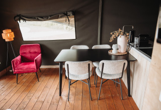 Intérieur de lodge moderne avec fauteuil rouge, table noire et quatre chaises claires à De Achterste Hoef.
