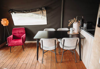 Intérieur de lodge moderne avec fauteuil rouge, table noire et quatre chaises claires à De Achterste Hoef.