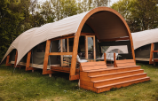 Alojamiento Water Lodge moderno con terraza de madera y techo curvo, rodeado de césped y árboles.