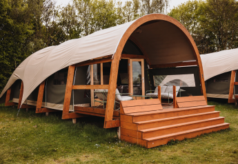 Water Lodge moderne avec terrasse en bois et toit courbé, entourée d’arbres et de verdure luxuriante.
