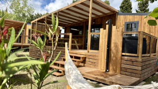 Wooden lodge at La Clairiere with a covered porch, hammock, and green plants in the foreground, sunny day.