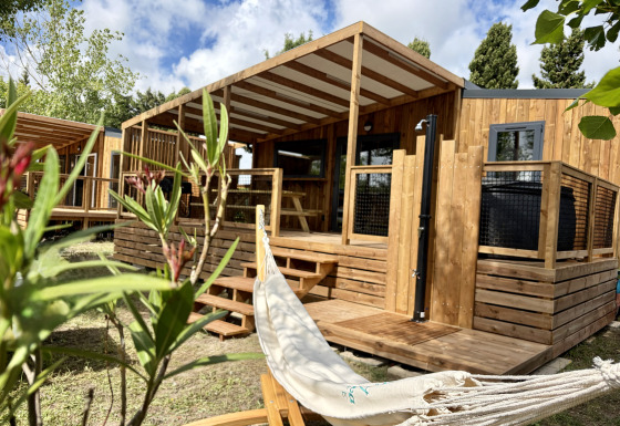 Lodge in legno a La Clairiere con veranda coperta, amaca e piante verdi in primo piano, giornata soleggiata.