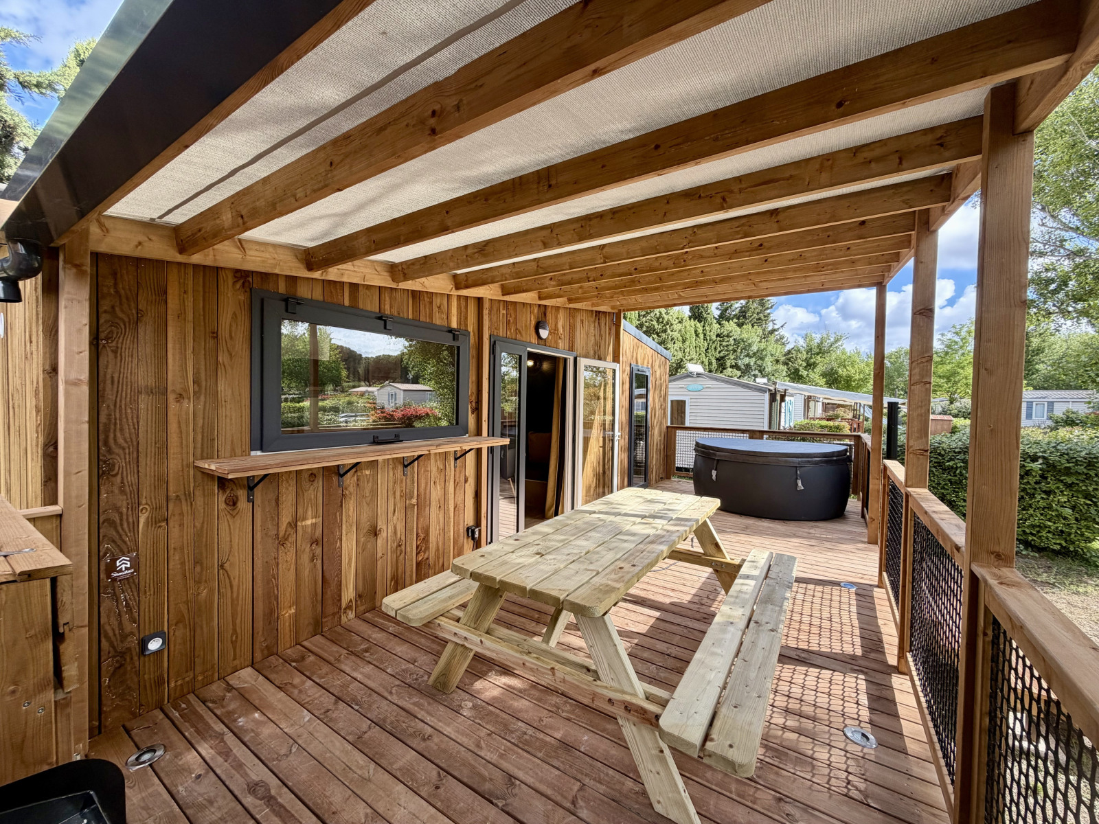 Overdekt houten terras met picknicktafel en hottub bij La Clairiere lodge, Camping Seasonova Ensoya, Frankrijk.