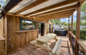Covered wooden terrace with picnic table and hot tub at La Clairiere lodge, Campsite Seasonova Ensoya, France.