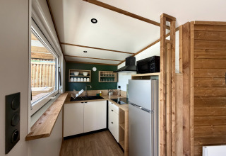 Modern, cozy kitchen in La Clairiere lodge at Campsite Seasonova Ensoya, France, featuring wood accents and appliances.