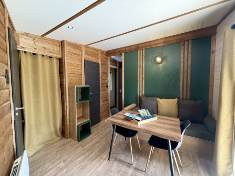 Interno di una lodge accogliente a La Clairiere, Campeggio Seasonova Ensoya, Francia, con pareti in legno, tavolo e divano.