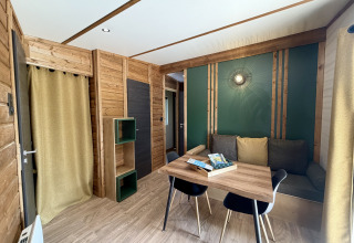 Interiørbillede af en hyggelig lodge på La Clairiere, Campsite Seasonova Ensoya, med trævægge, spisebord og sofa.